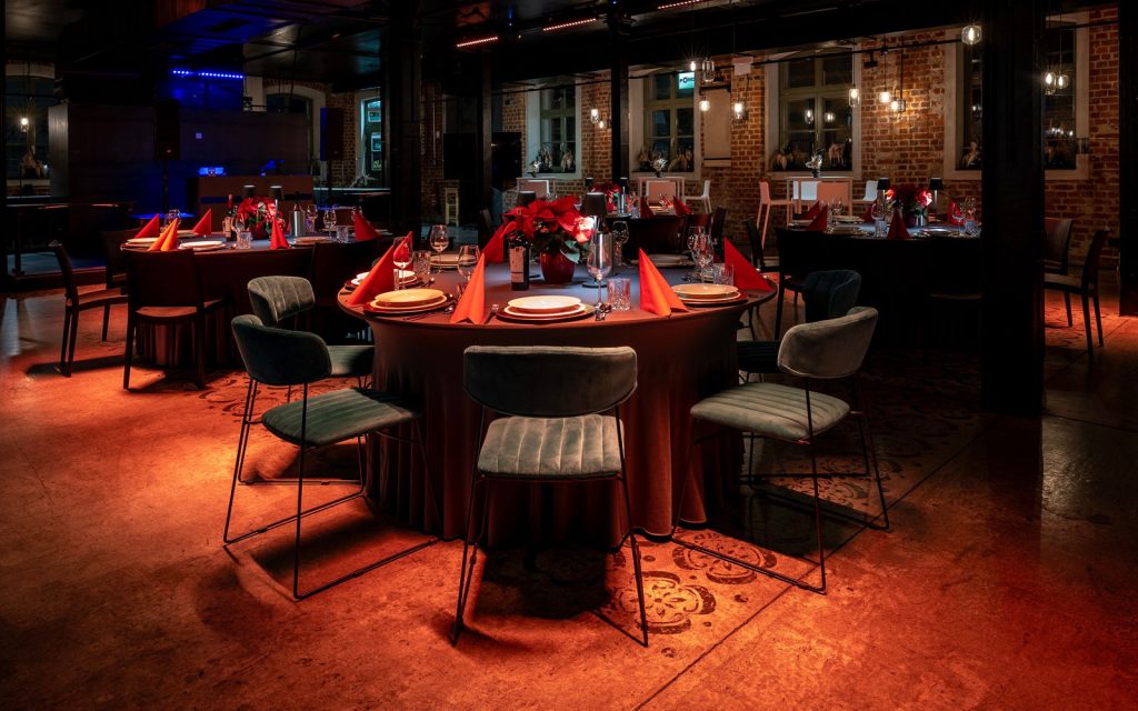 EVENTGIESSEREI Weihnachtsfeier Setup mit runden, festlich gedeckten Banketttischen und Bankettstühlen, weihnachtlicher Ambientebeleuchtung.
