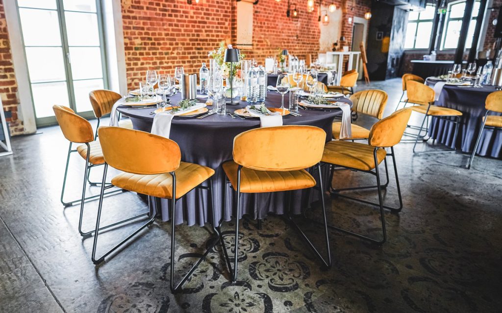 Banketttisch mit dunkler Husse, goldene Stühle, im Hintergrund rote Ziegelwände