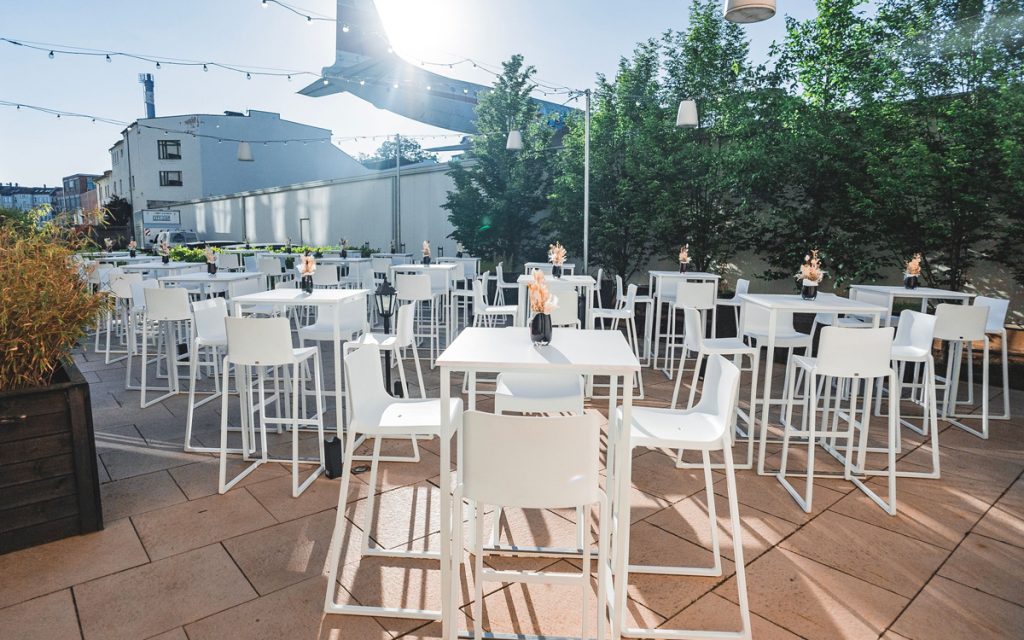 Außenbereich der EVENTGIESSEREI Eventlocation Leipzig mit weißen Stehtischen und Barhockern, im Hintergrund das Flugzeug IL-18