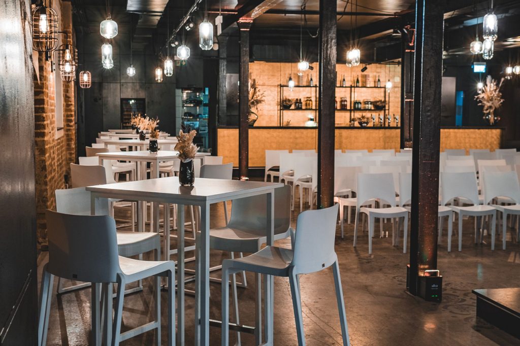 Setup für Marken-Events mit weißen Stehtischen und Barhockern vor goldener Bar