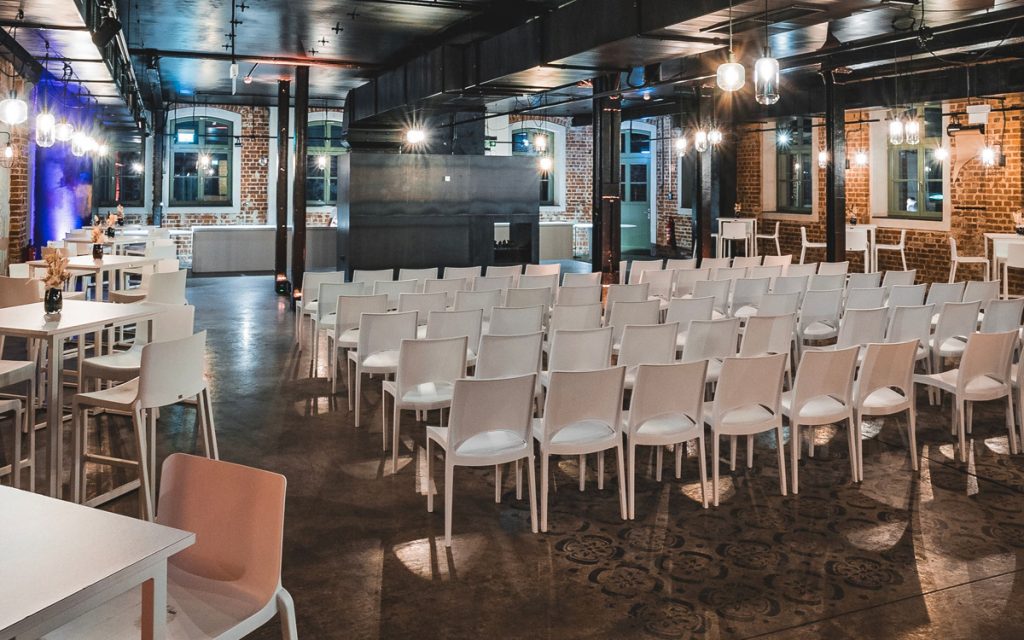 Tagung-Setup in der EVENTGIESSEREI mit weißen Stühlen in Reihen vor kleiner Bühne